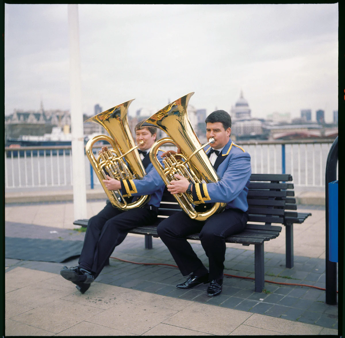Two Williams Fairey Band tuba players seated with their instruments on the Southbank in London in 1997