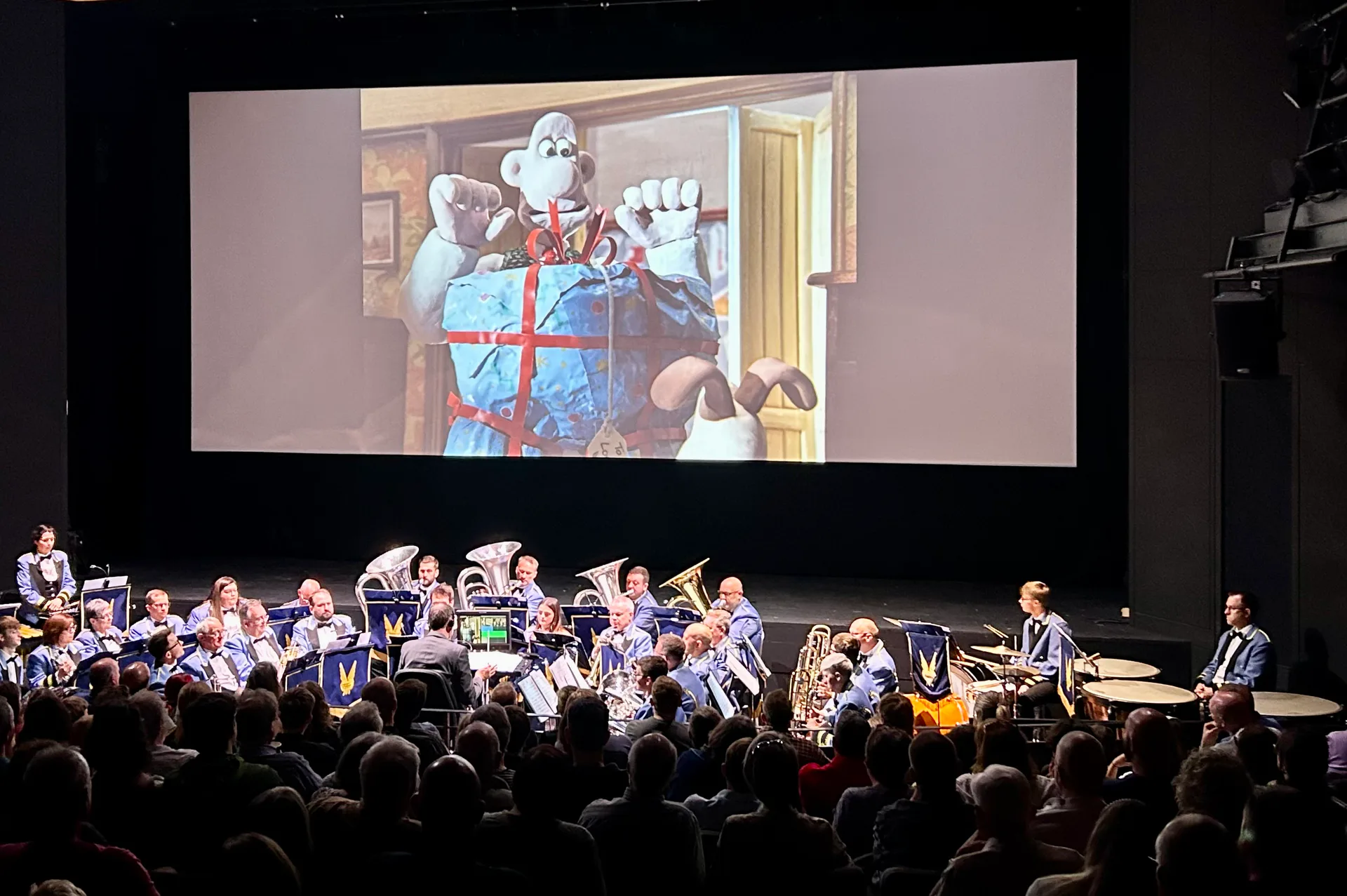 The KNDS Fairey Band performing a Wallace and Gromit score beneath a cinema screen