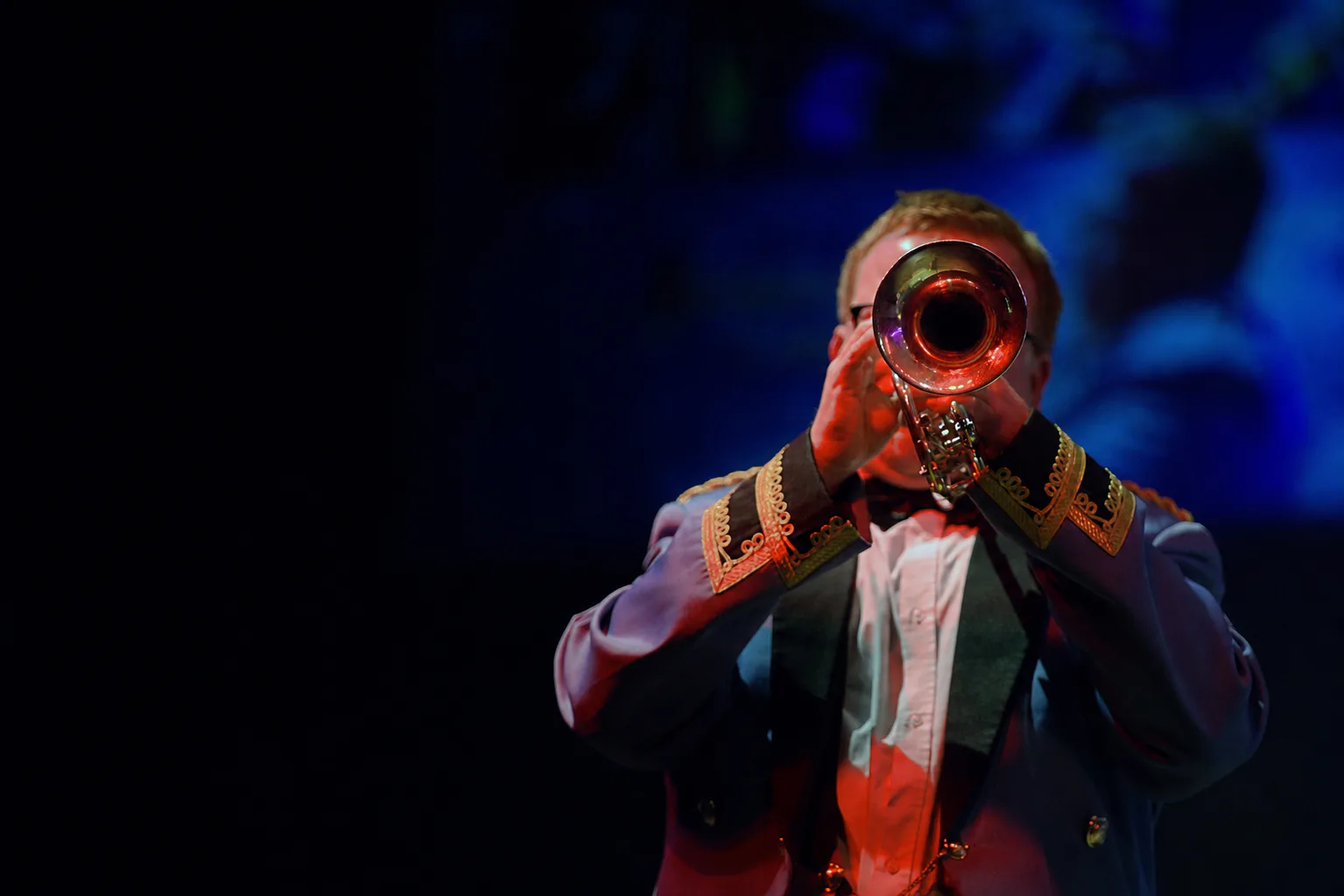 A KNDS Fairey Band trumpet player performing under blue and red stage lighting